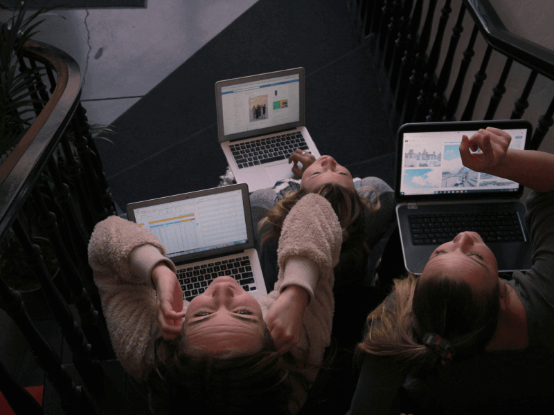 3 people working on laptops sat on a stairwell