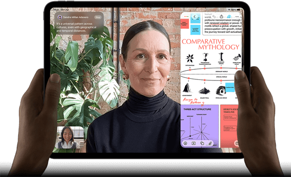 iPad Pro, front exterior, landscape orientation, space black colour, rounded corners, black display bezel, hands holding left and right sides, display showing a FaceTime conversation being live translated, and an educational app showing a presentation of Comparative Mythology with text, diagrams and handwritten notes