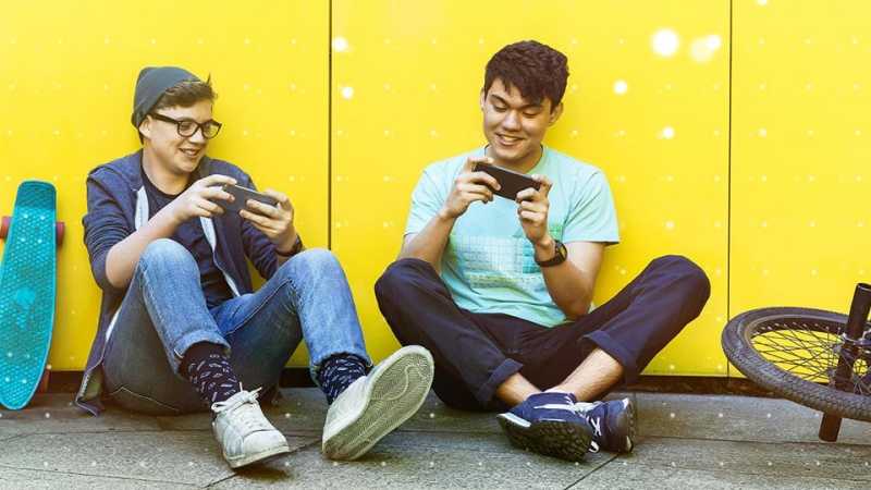 Two young men sat on the pavement playing games on their mobile phones