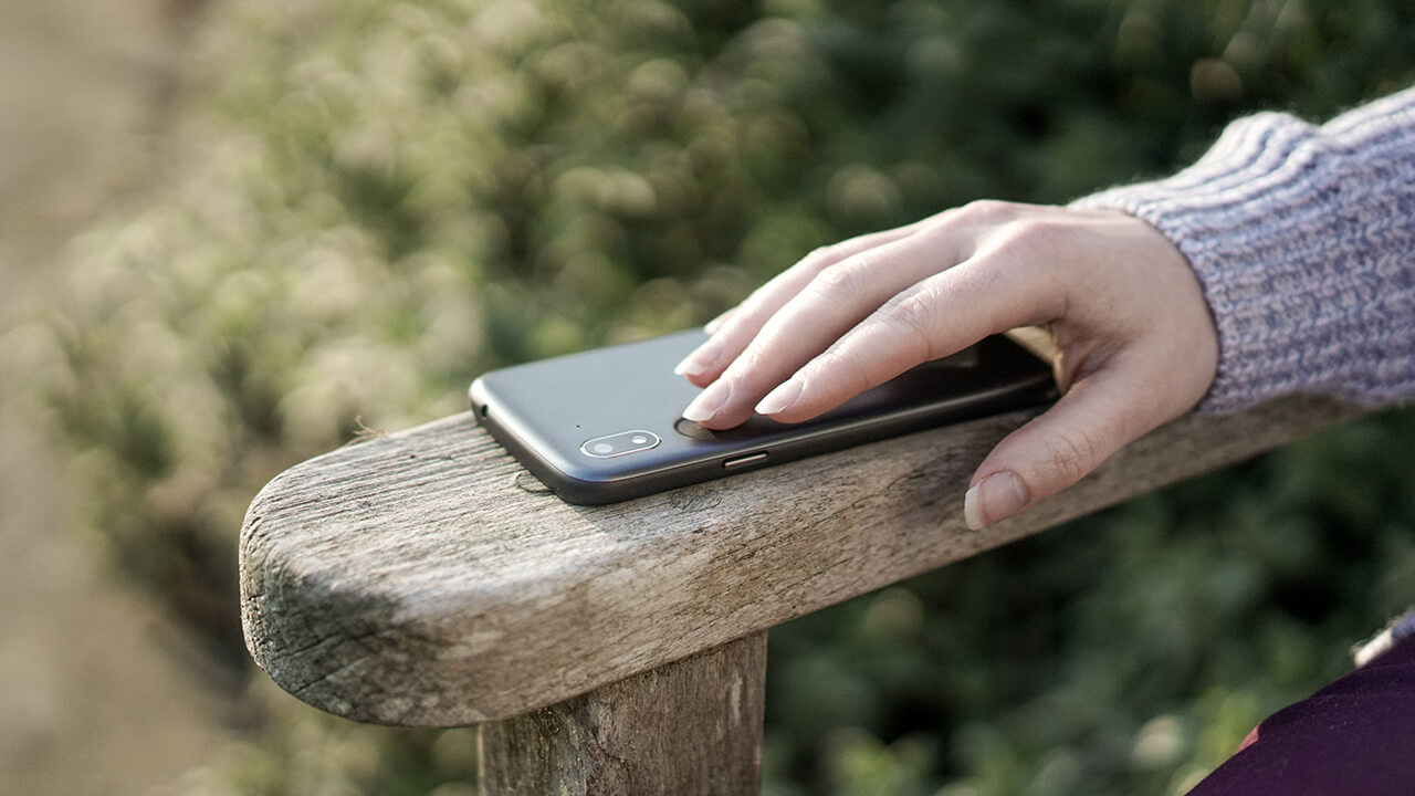 a woman's hand on top of the Response button on a Doro phone while sitting on an outside bench