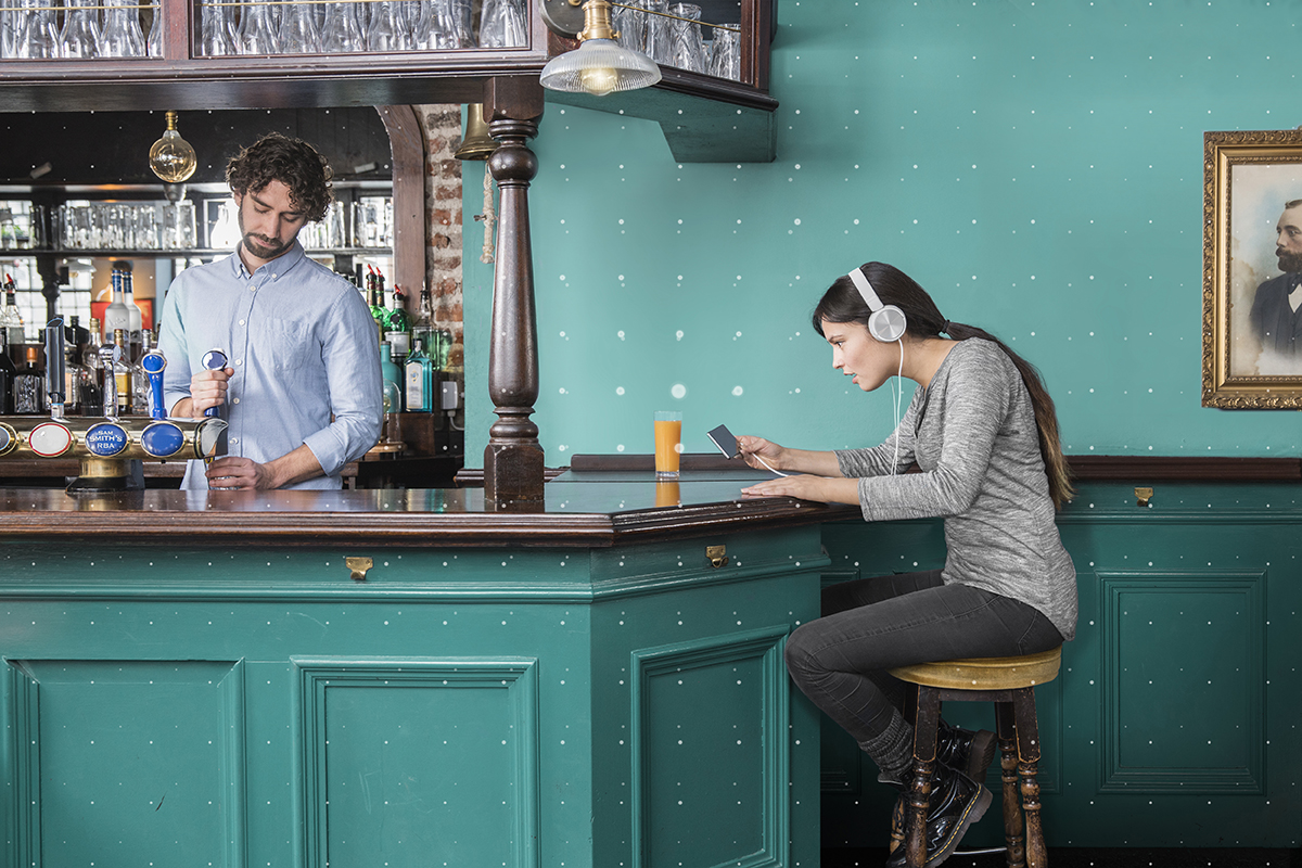 woman in a bar wearing headphones and watching her phone