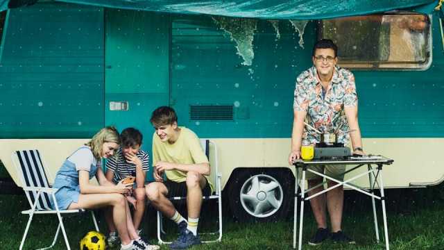 A family taking cover from the rain under a caravan awning looking at an EE smartphone