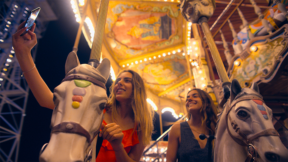 two girls taking a selfie while sitting on the horses on a merry-go-round