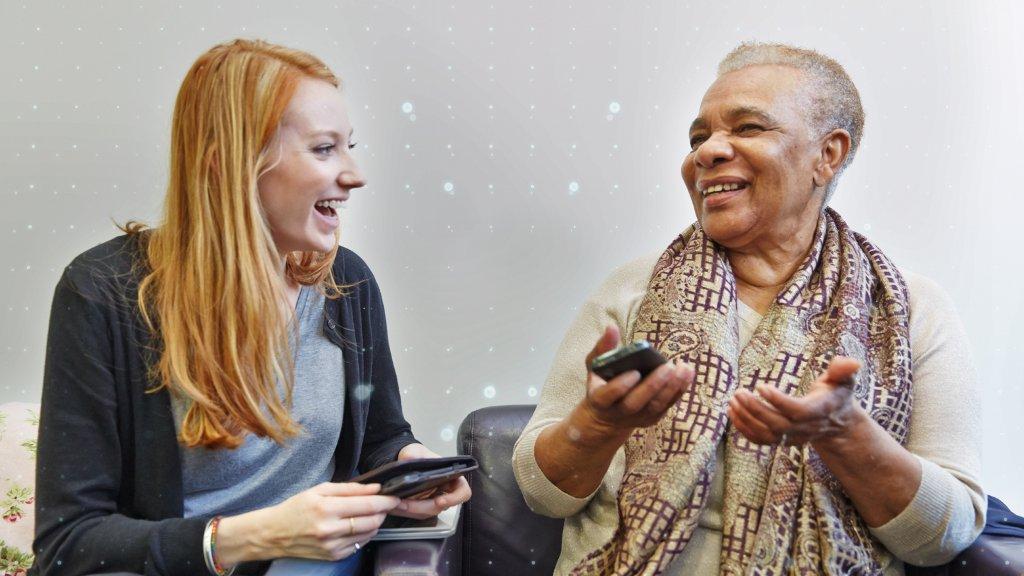 Two ladies laughing holding smartphones while learning how to use and get them most from the devices