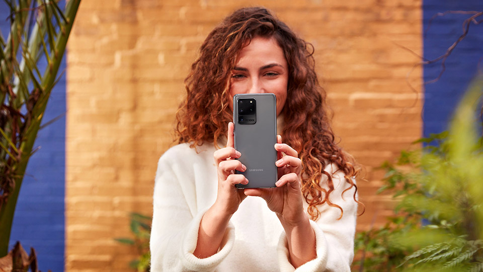 a woman with curly brown hair holding up her Samsung Galaxy Ultra 5G in both hands to take a photo