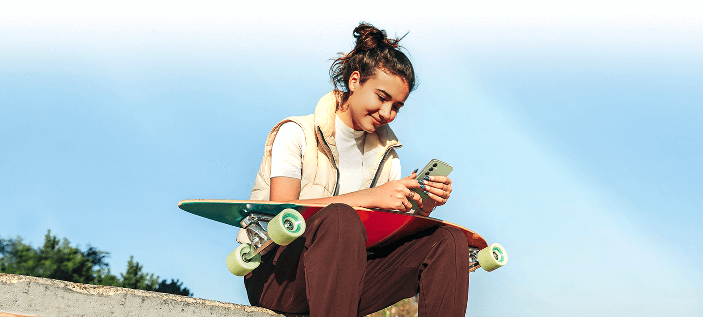 A young woman sat outside with a skateboard on her lap, enjoying content on the bright screen of the A54 5G