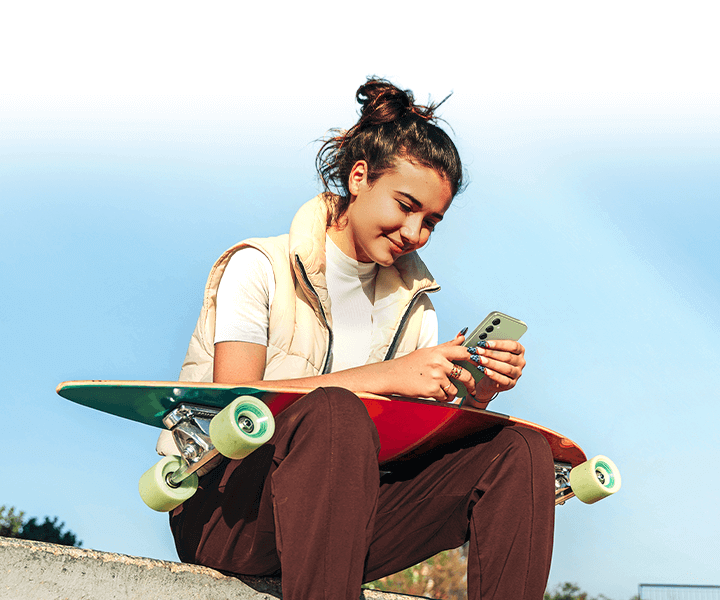 A young woman sat outside with a skateboard on her lap, enjoying content on the bright screen of the A54 5G