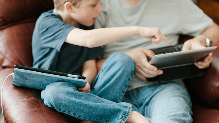 A young boy sat on his father's lap, looking at a tablet