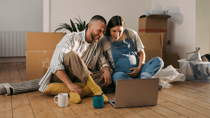 A pregnant woman and her partner looking at a laptop in their new home