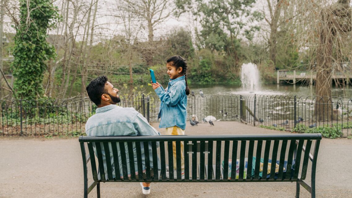 A young girl using a smartphone to take a picture of her Dad at the park