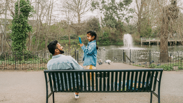 A young girl playing on a smartphone while at the park with her Dad